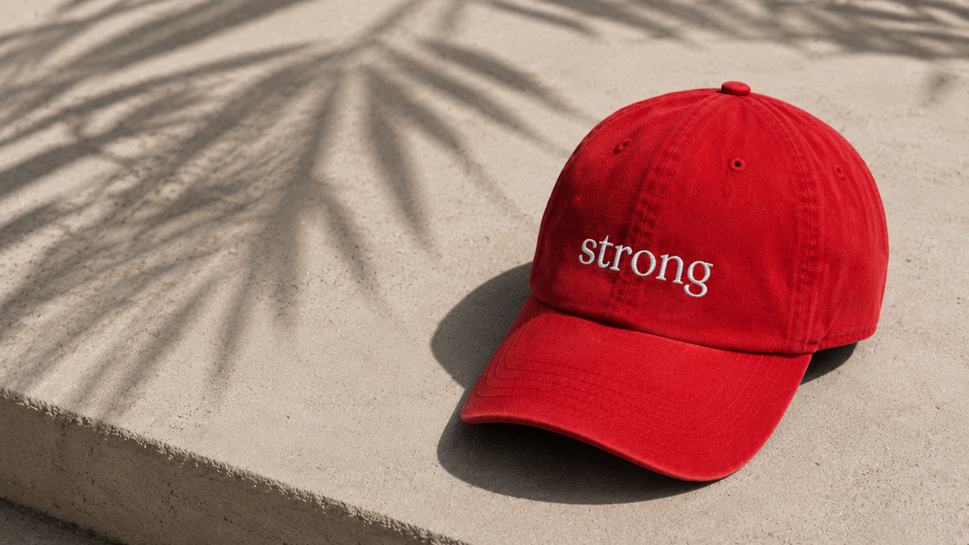 Red cap with 'strong' text on a sandy surface with palm leaf shadows