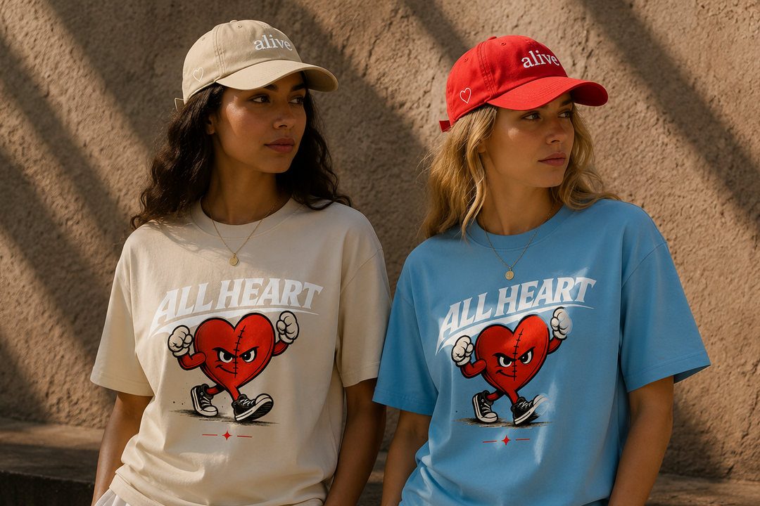 Two people wearing 'All Heart' t-shirts with a red heart design against a textured wall.
