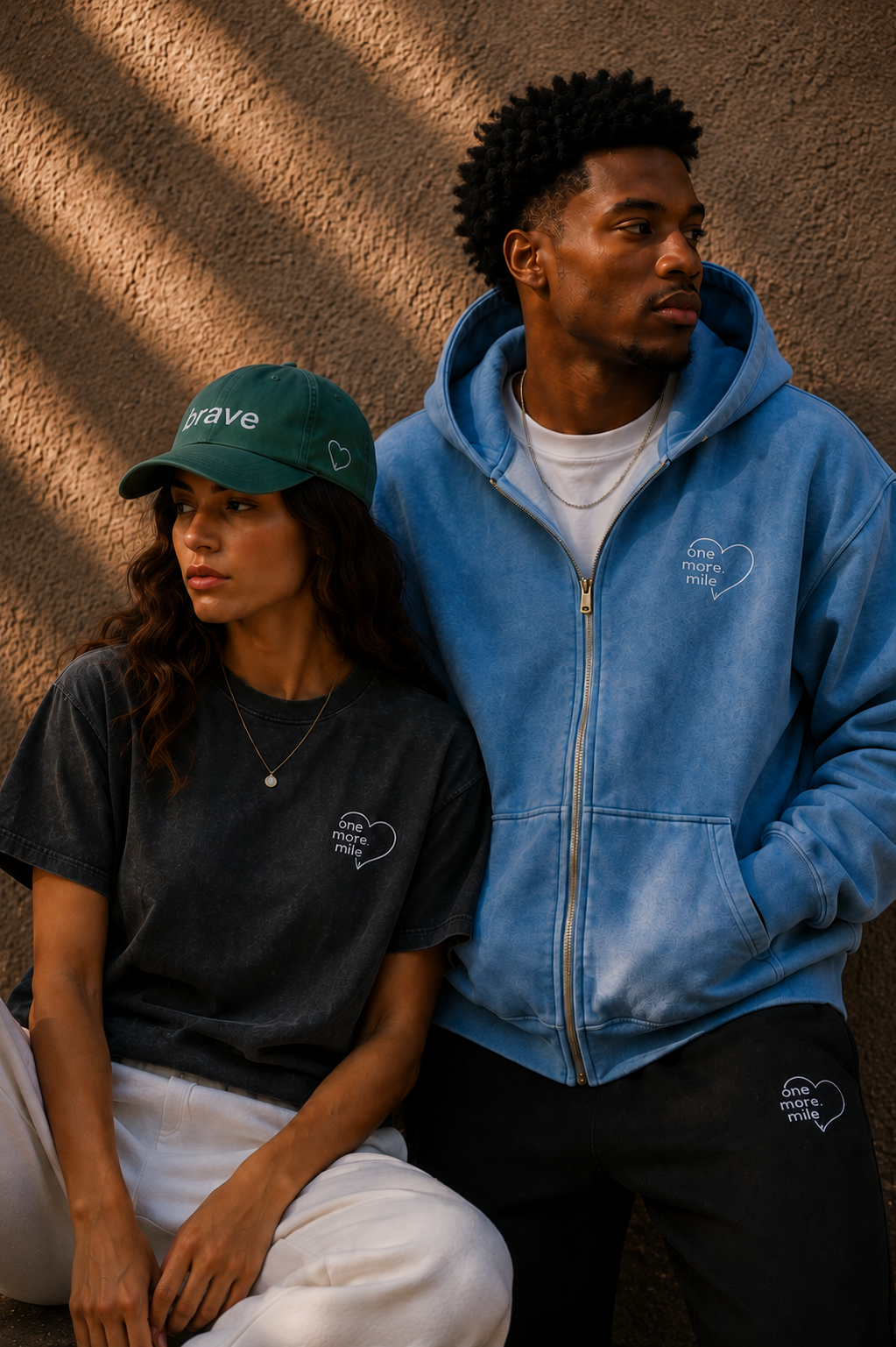 Two people wearing branded clothing against a textured wall.