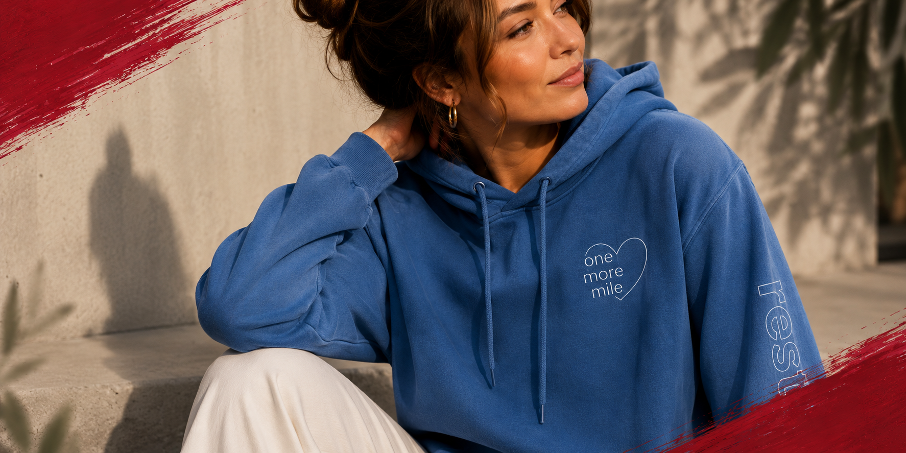 Woman wearing a blue hoodie with text, sitting against a wall.
